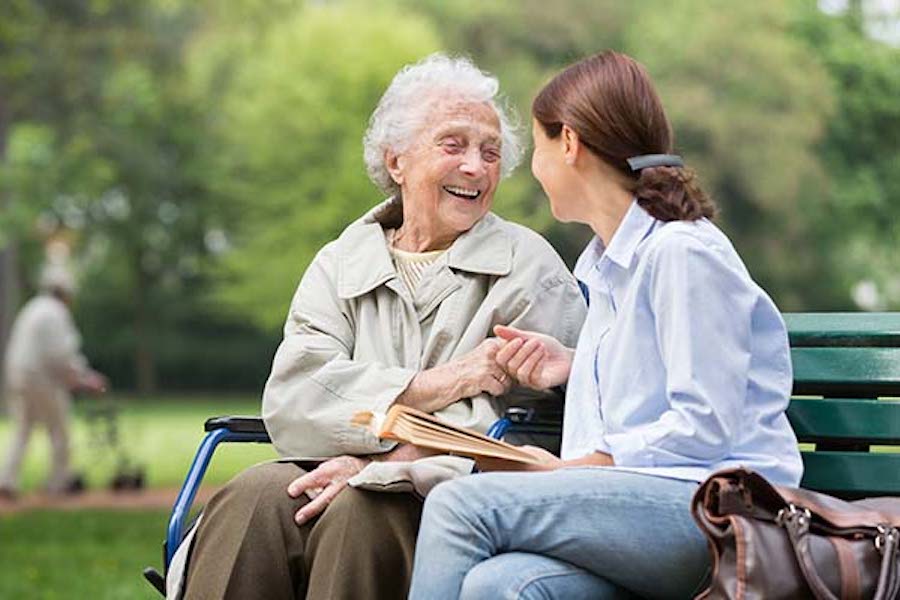 An older woman and younger woman laughing together on a park bench