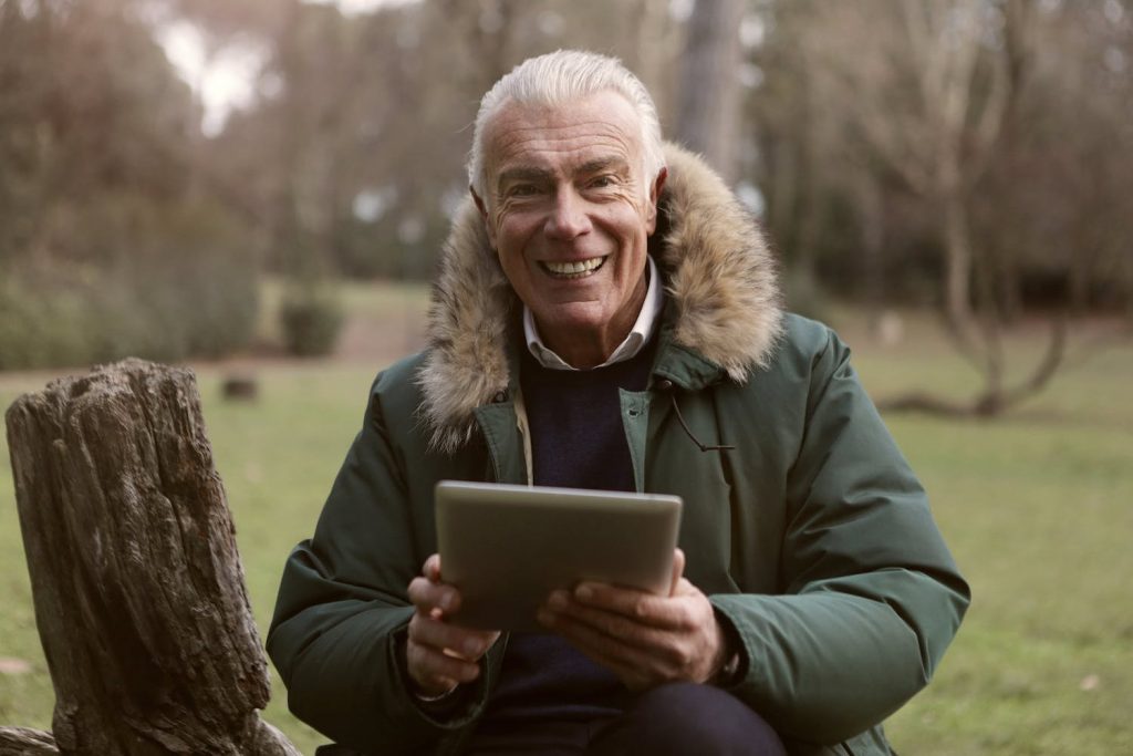 An elderly man using a tablet and smiling in a park setting