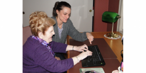 A younger woman instructing an older adult on a computer keyboard