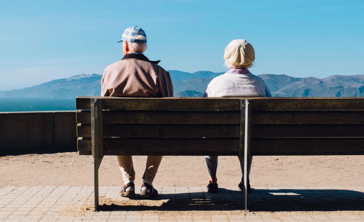 Two elderly adults sitting on a bench looking out at the mountains
